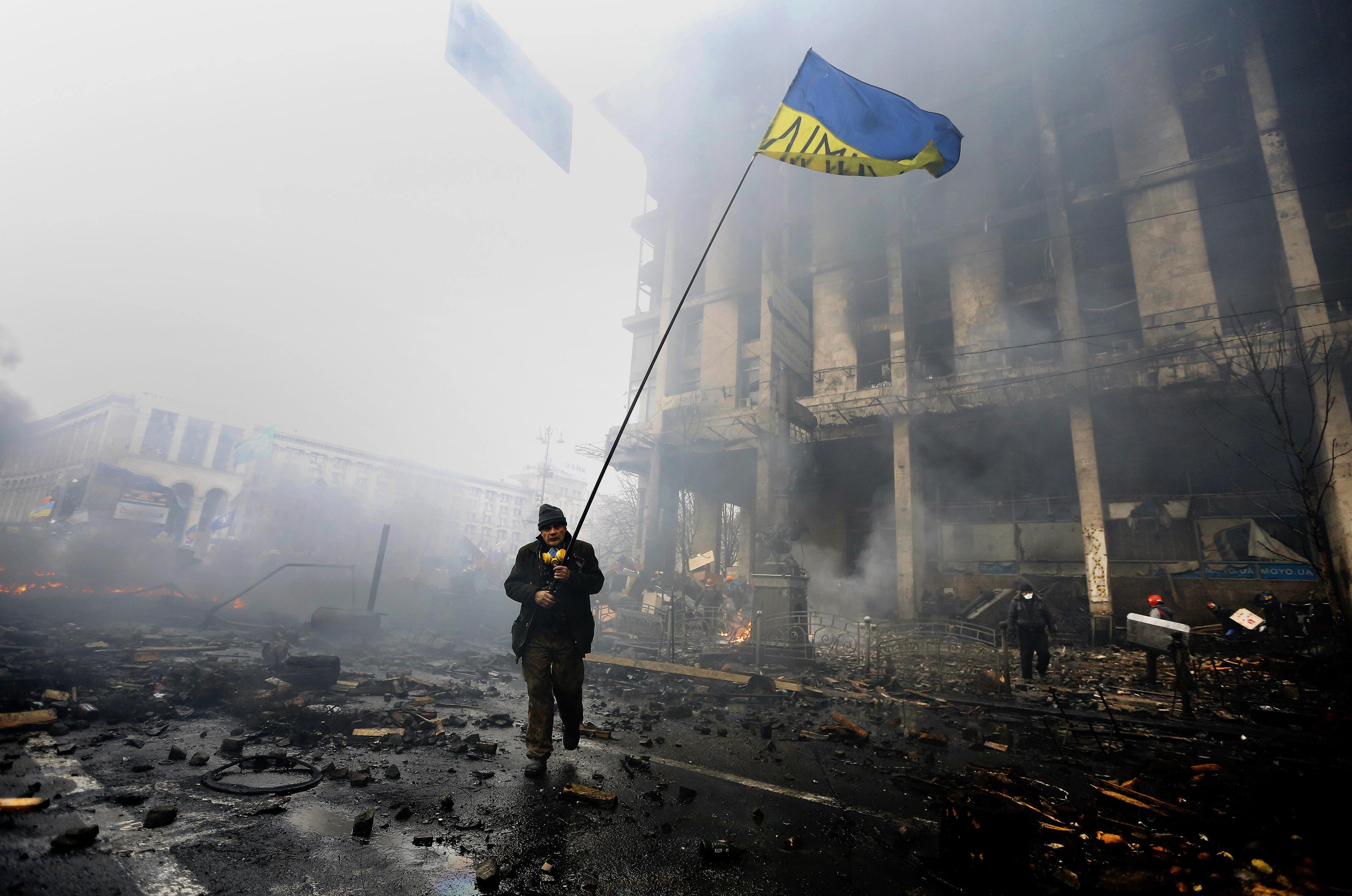 An anti-government protester holds a Ukranian flag as he advances through burning barricades in Kiev